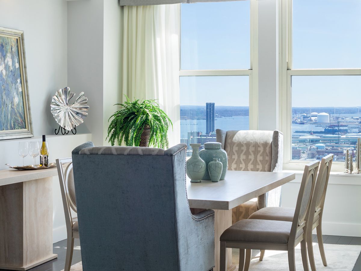 A bright dining room with a table, chairs, decorative vases, a plant, and large windows showcasing a stunning view outside.