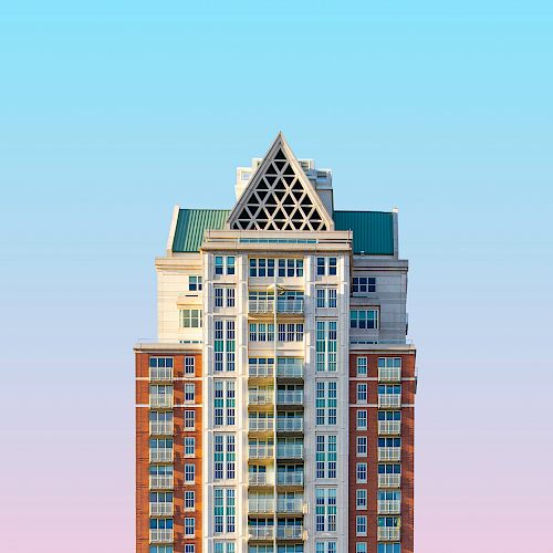 A tall building with a mix of brick and white facade, featuring a unique triangular roof, set against a gradient sky.