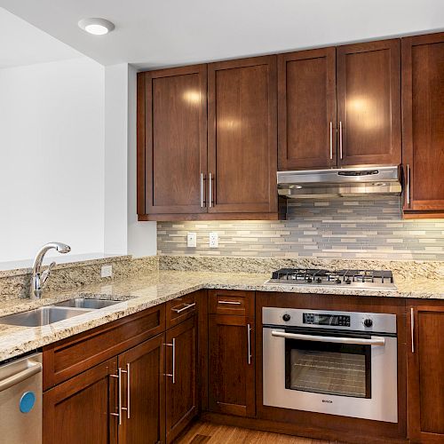 A modern kitchen with dark wood cabinets, granite countertops, a stainless steel oven, and a dishwasher, with a tile backsplash.