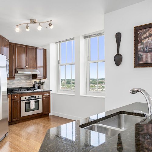 A modern kitchen with wooden cabinets, stainless steel appliances, granite countertops, and large windows with a scenic view.