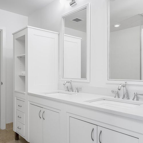 A modern bathroom with white cabinets, dual sinks, two mirrors, and overhead lighting fixtures, set against a clean, minimalist design background.