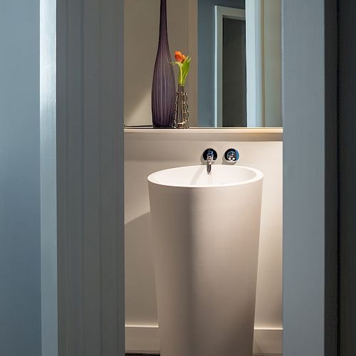 A modern bathroom with a tall, cylindrical sink and a vase with flowers on the counter in the background.