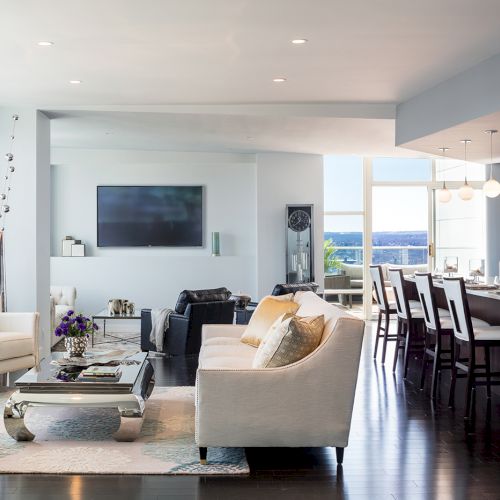 A modern open-plan living room and kitchen with light-colored furniture, large windows, and a flat-screen TV on the wall ends the sentence.