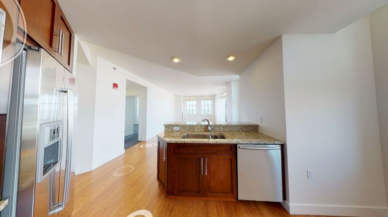 The image shows a modern kitchen with a stainless steel fridge, dishwasher, microwave, wooden cabinets, granite countertops, and hardwood floors.