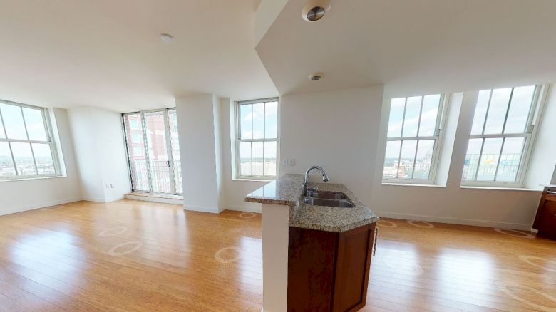 A spacious, sunlit apartment with large windows, wooden floors, a kitchen with modern appliances, and an open living area.