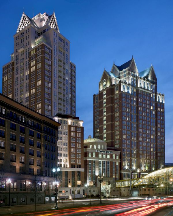 The image depicts tall, illuminated buildings during twilight, with blurred car lights in the foreground, suggesting a bustling urban environment.